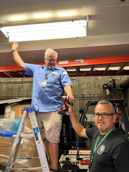 Two City employees working together to fix a light in the ceiling.